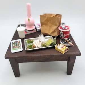 May include: A miniature wooden table with a pink glass bong, a brown paper bag, a red and white KFC cup, a silver tray with green leafy material and white sticks, a white cell phone, a white cup with a straw, a magazine, a pack of Camel cigarettes, and a small ashtray with a cigarette butt.
