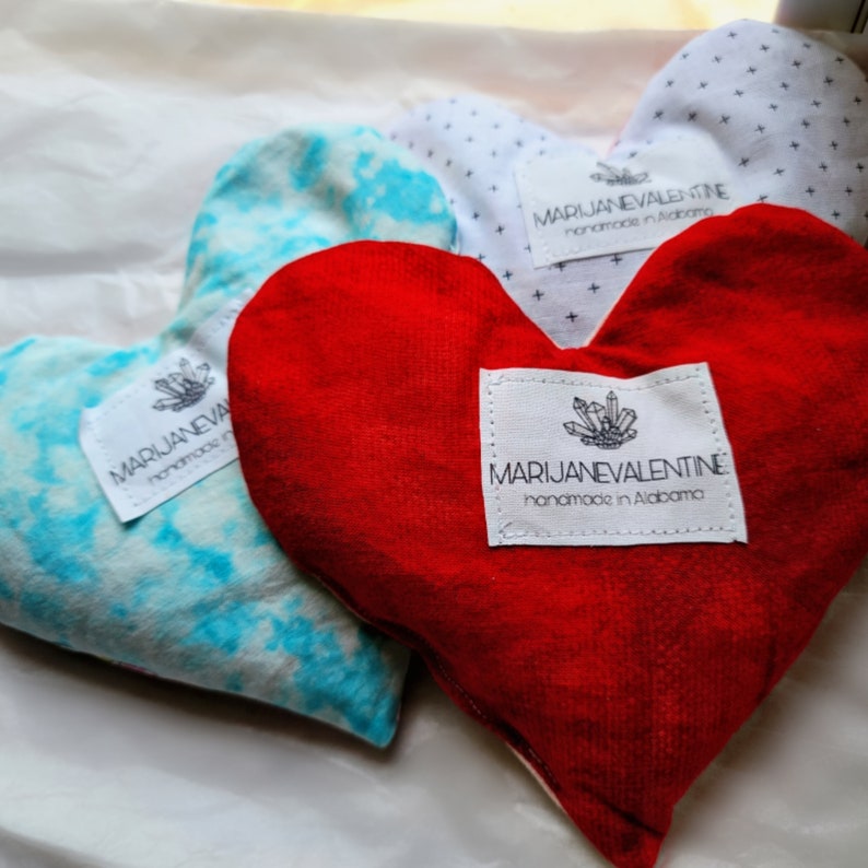 May include: Three heart-shaped pillows with tie-dye, white with black polka dots, and red fabric. Each pillow has a white label with the text "MARIJANEVALENTINE handmade in Alabama".