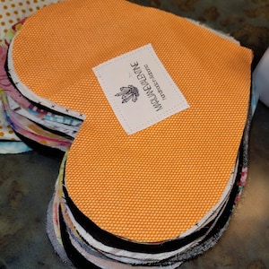 May include: A stack of orange fabric heart shapes with a white label that says "MADJANEVALINE" and "handmade in victoria" in black text.
