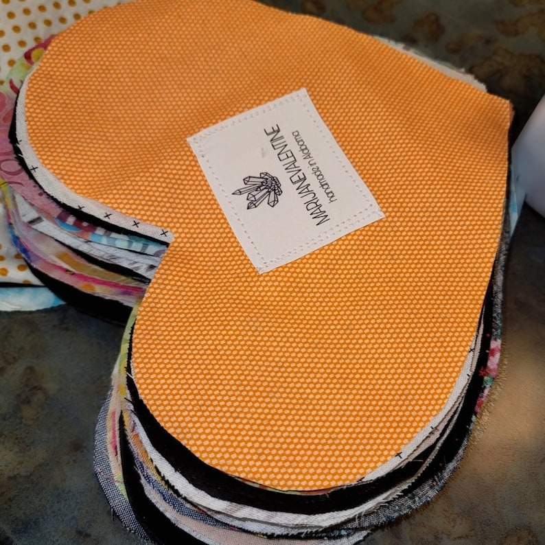 May include: A stack of orange fabric heart shapes with a white label that says "MADJANEVALINE" and "handmade in victoria" in black text.