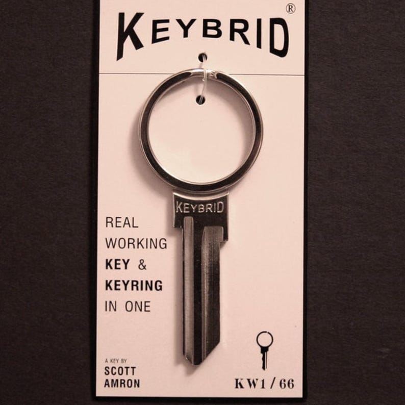 K&ouml;nnte beinhalten: Ein silberner Schl&uuml;ssel mit einem Schl&uuml;sselring, der oben befestigt ist. Der Schl&uuml;ssel tr&auml;gt die Aufschrift "KEYBRID" und "REAL WORKING KEY & KEYRING IN ONE". Der Schl&uuml;ssel ist auf einer wei&szlig;en Karte verpackt, auf der "A KEY BY SCOTT AMRON" und "KW1/66" aufgedruckt sind.