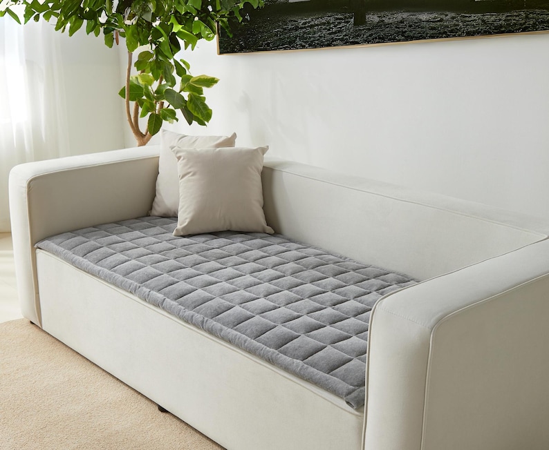 May include: A white couch with a gray quilted cushion on top. The couch has a white fabric covering and a simple design.