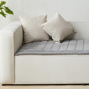 May include: A white couch with a gray quilted cushion. Two white pillows are on the couch.