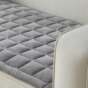 May include: Gray quilted sofa protector with a diamond pattern. The protector is placed on a white sofa.