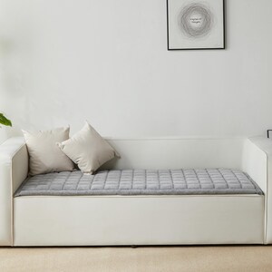 May include: A white sofa bed with a gray quilted mattress and two white pillows. The sofa bed is against a white wall with a framed print above it.