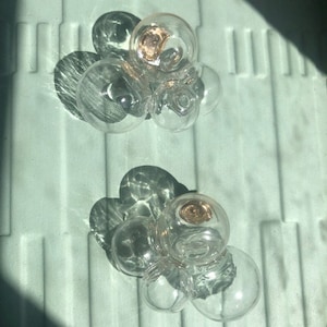 May include: A set of five clear glass spheres, each with a slightly different shape and size, arranged in a cluster. The spheres are illuminated from above, creating a shimmering effect.