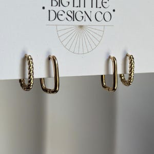 May include: Four gold-toned hoop earrings attached to a white display card featuring the text BIG LITTLE DESIGN CO. The set includes two rectangular hoops with a smooth finish and two rectangular hoops with a twisted rope-like texture.