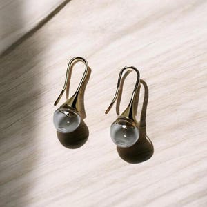 May include: A pair of gold drop earrings with clear glass teardrop-shaped pendants.