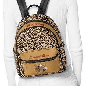 May include: A tan and black leopard print backpack with black straps. The backpack has a front pocket with the text "Baseball Mom" and a baseball bat and ball graphic. The top of the backpack has the text "YOUR TEAM".