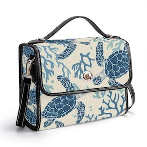 以下が含まれることがあります： 黒いハンドルとストラップが付いた長方形のハンドバッグ。バッグは、青いウミガメとサンゴのパターンが施されたクリーム色の背景が特徴です。エッジは黒でトリミングされ、バッグにはシルバーの留め金が付いています。