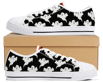May include: White canvas sneakers with a black background and a repeating pattern of white cartoon ghosts. The shoes have white laces, a white rubber sole, and a black stripe along the bottom.