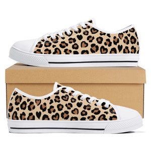 May include: White canvas low-top trainers with a leopard print pattern featuring brown and black spots and hearts.