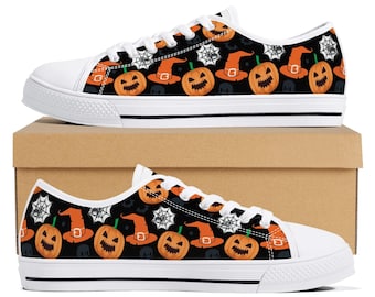 May include: White canvas sneakers with a black Halloween-themed pattern. The pattern includes orange jack-o'-lanterns, witch hats, and spiderwebs. The shoes have white laces, soles, and toe caps, and are displayed on a brown cardboard box.