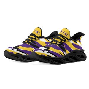 May include: A pair of trainers with a black sole and a patterned upper. The upper features yellow, purple, and white shapes. The word "TIAL" is printed on the side of each shoe.