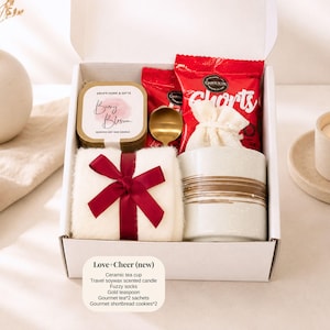 Pu&ograve; includere: Una confezione regalo con una tazza da t&egrave; in ceramica, una candela profumata alla cera di soia, calzini pelosi, un cucchiaino dorato, bustine di t&egrave; gourmet e biscotti shortbread. La scatola include un asciugamano bianco legato con un fiocco rosso. La scatola &egrave; etichettata "Love + Cheer (new)".