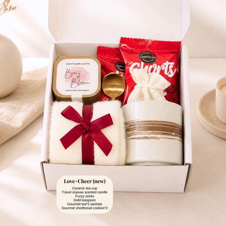 Pu&ograve; includere: Una confezione regalo con una tazza da t&egrave; in ceramica, una candela profumata alla cera di soia, calzini pelosi, un cucchiaino dorato, bustine di t&egrave; gourmet e biscotti shortbread. La scatola include un asciugamano bianco legato con un fiocco rosso. La scatola &egrave; etichettata "Love + Cheer (new)".