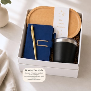 Pu&ograve; includere: Confezione regalo con un taccuino blu, penna dorata, bicchiere nero e vassoio in legno. La scatola include il testo "For Every Occasion" e "Desktop Essentials". Gli articoli sono in una scatola bianca.