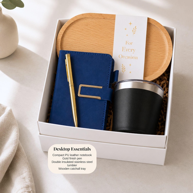 Pu&ograve; includere: Confezione regalo con un taccuino blu, penna dorata, bicchiere nero e vassoio in legno. La scatola include il testo "For Every Occasion" e "Desktop Essentials". Gli articoli sono in una scatola bianca.