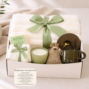 Pu&ograve; includere: Una confezione regalo con una coperta in pile, una tazza in ceramica, una candela e altri oggetti accoglienti. La scatola &egrave; legata con un nastro verde. Una piccola carta dice "Shea & Mint". La scatola &egrave; etichettata "Blanket Box: Everyday Cozy".