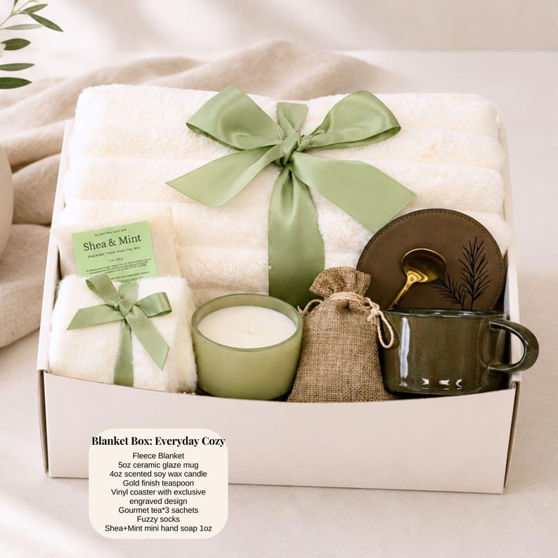 Pu&ograve; includere: Una confezione regalo con una coperta in pile, una tazza in ceramica, una candela e altri oggetti accoglienti. La scatola &egrave; legata con un nastro verde. Una piccola carta dice "Shea & Mint". La scatola &egrave; etichettata "Blanket Box: Everyday Cozy".