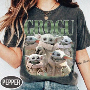 May include: Dark gray t-shirt featuring the word "GROGU" in green, with a graphic of Grogu from The Mandalorian. The graphic shows Grogu in various poses. The shirt has a vintage, worn look.