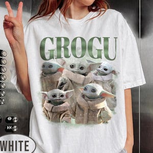 May include: White t-shirt featuring the word "GROGU" in green block letters above a graphic of Grogu, also known as Baby Yoda, from the Star Wars series. The graphic shows multiple images of Grogu.