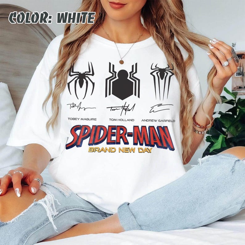 May include: White t-shirt featuring three black spider emblems and the text "SPIDER-MAN BRAND NEW DAY". The shirt also includes the names of Tobey Maguire, Tom Holland, and Andrew Garfield.