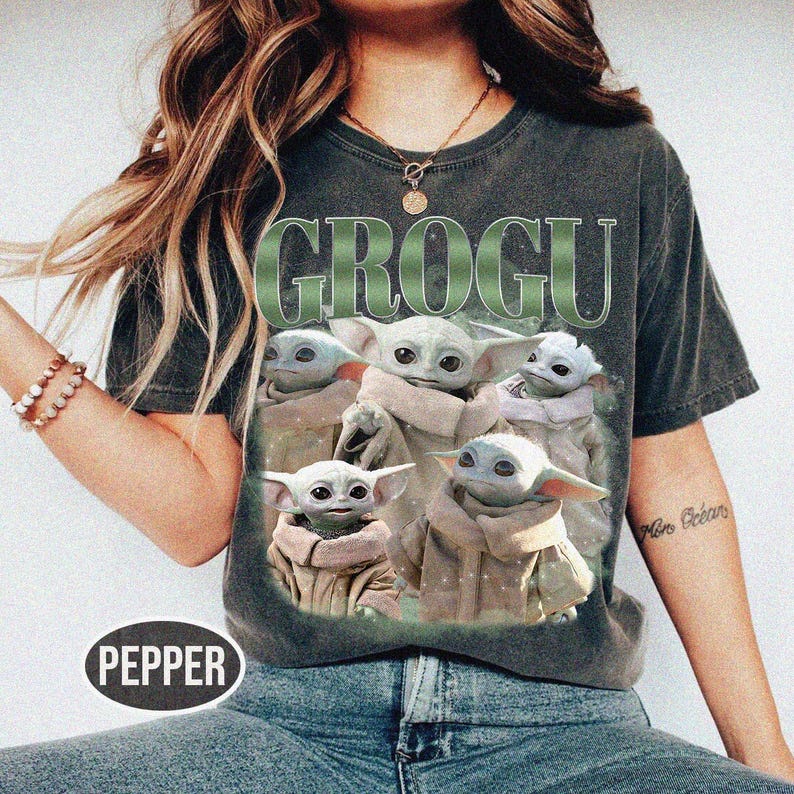 May include: Dark gray t-shirt featuring the word "GROGU" in green, with a graphic of Grogu from The Mandalorian. The graphic shows Grogu in various poses. The shirt has a vintage, worn look.