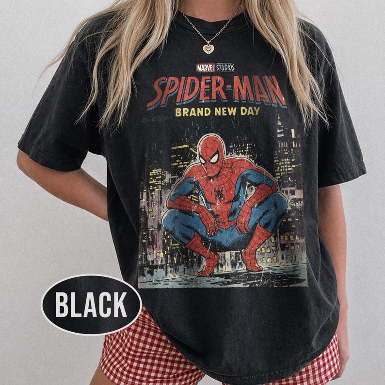 Może przedstawiać: Czarny t-shirt z wytartą grafiką Spider-Mana w kucającej pozie na tle miasta. Koszulka zawiera napis "MARVEL STUDIOS SPIDER-MAN BRAND NEW DAY".
