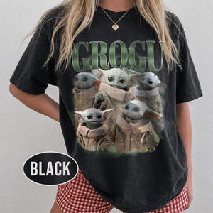 May include: Black t-shirt featuring a graphic of Grogu, also known as Baby Yoda, surrounded by multiple images of himself. The word "GROGU" is printed in green above the images. A black oval with the word "BLACK" is at the bottom.