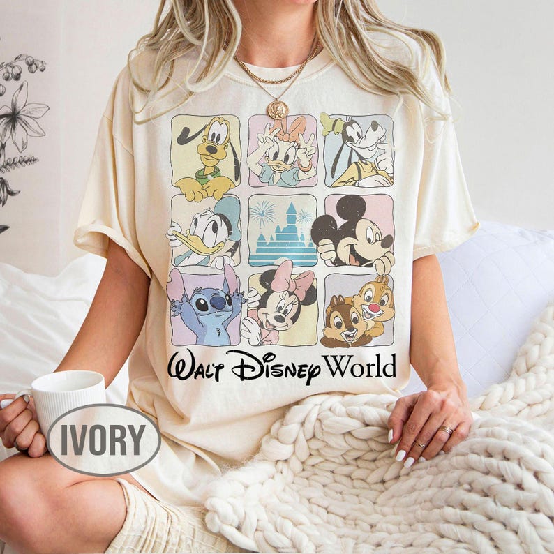 May include: An ivory t-shirt featuring a grid of nine squares, each containing a different Disney character or the castle, with the text Walt Disney World printed in black below the grid. The characters include Pluto, Daisy, Goofy, Donald, Mickey, Stitch, Minnie, Chip, and Dale.