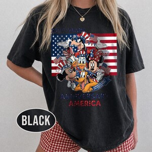 以下が含まれることがあります： アメリカ国旗を背景に、ディズニーキャラクターが描かれた黒いTシャツ。デザインにはミッキーマウス、ミニーマウス、ドナルドダック、グーフィー、プルートが含まれ、「250 Years Anniversary America」の文字があります。