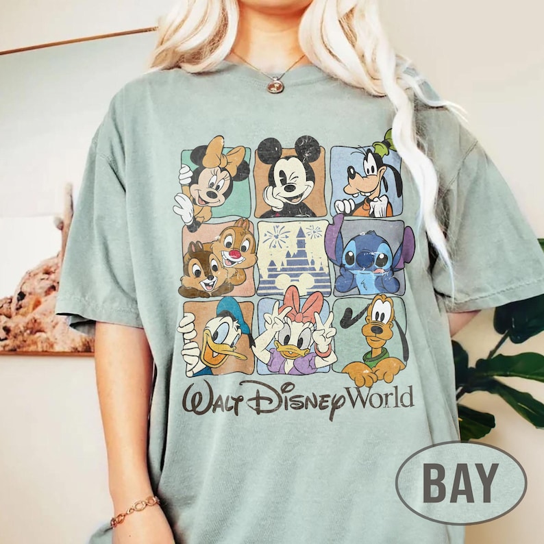 Op de afbeelding: Saliegroen t-shirt met een raster van Disney-personages, waaronder Mickey Mouse, Minnie Mouse, Donald Duck en Stitch. De woorden "Walt Disney World" zijn gedrukt in een vintage lettertype. Een casual, comfortabel t-shirt.