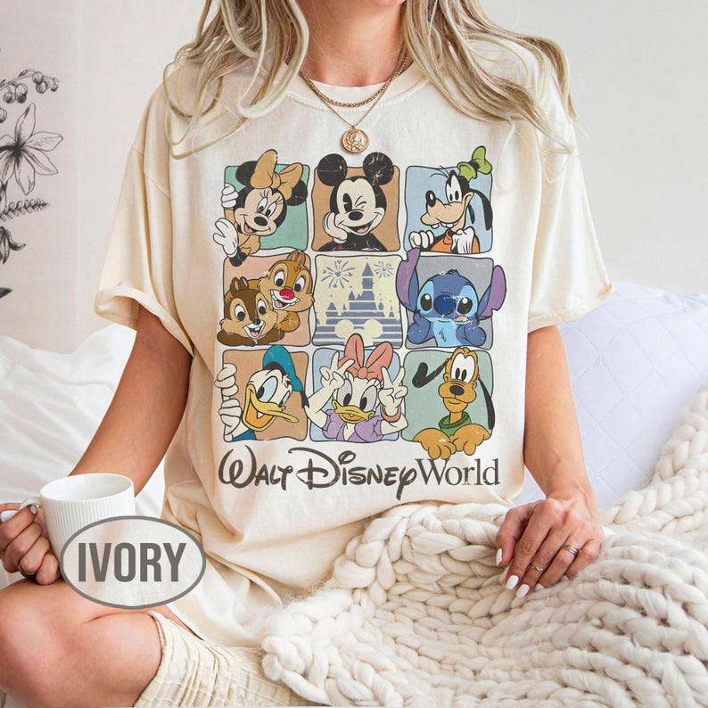 Op de afbeelding: Ivoor kleurig t-shirt met een raster van Disney-personages, waaronder Mickey Mouse, Minnie Mouse, Goofy, Donald Duck, Daisy Duck, Chip en Dale, Stitch en Pluto. De woorden "Walt Disney World" staan eronder.