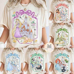 May include: Cream-colored t-shirts featuring various princess-themed designs. Each shirt showcases a different princess with a castle illustration, framed by a decorative border. The designs include Rapunzel, Moana, Tiana, Elsa, Mulan, and Merida.