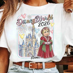 May include: White t-shirt featuring a colorful graphic of Miss Piggy in a red dress, standing in front of Cinderella's castle. The text "Disney World 2026" is above the image, with space for a name below.