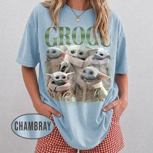 May include: Light blue t-shirt featuring a graphic of Grogu from The Mandalorian. The word "GROGU" is printed in green above the image of Grogu. The shirt is a light blue color.