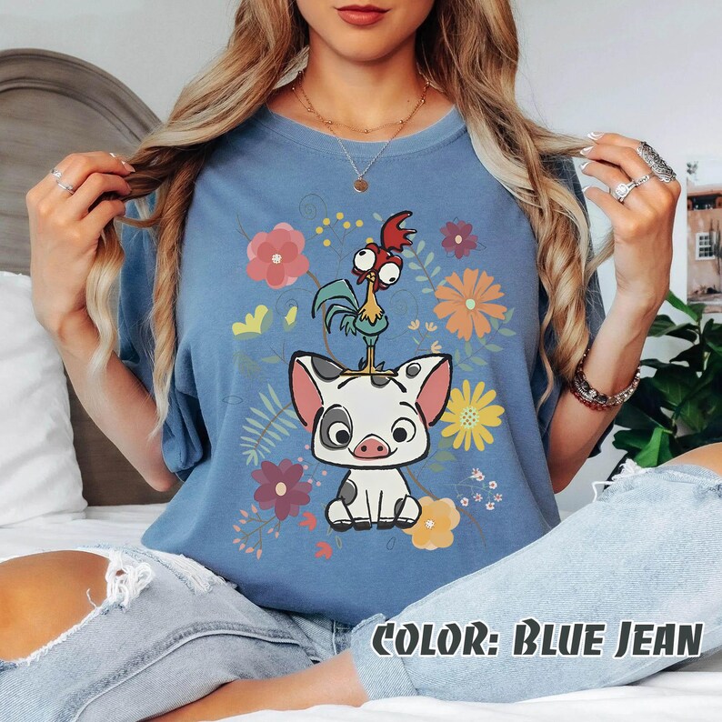 Puede incluir: Camiseta azul vaquero con un cerdo y un gallo de dibujos animados con detalles florales. El cerdo tiene manchas negras y el gallo tiene detalles rojos, amarillos y verdes. El texto "COLOR: BLUE JEAN" est&aacute; en la parte inferior.