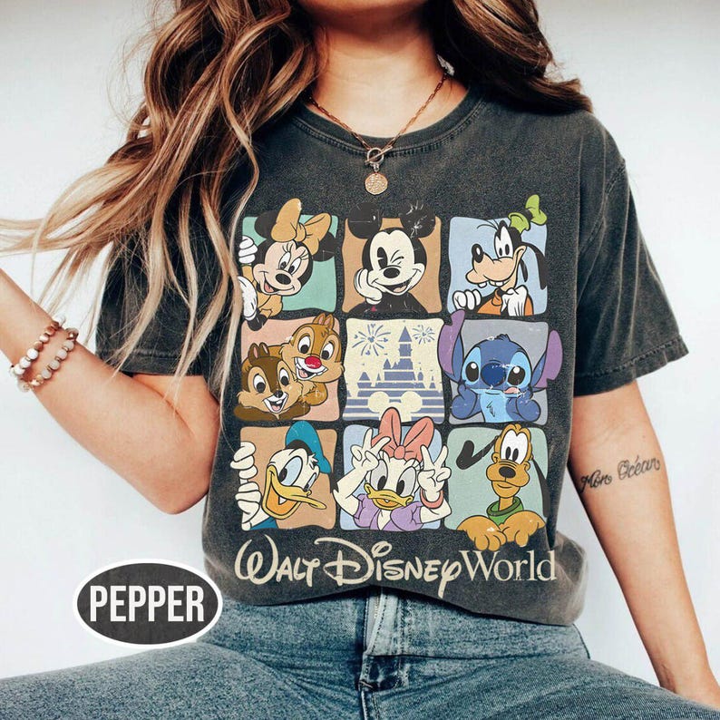 Op de afbeelding: Donkergrijs T-shirt met een raster van Disney-personages, waaronder Mickey Mouse, Minnie Mouse, Goofy en Stitch. De tekst "Walt Disney World" staat eronder gedrukt. Het woord "PEPPER" staat linksonder.