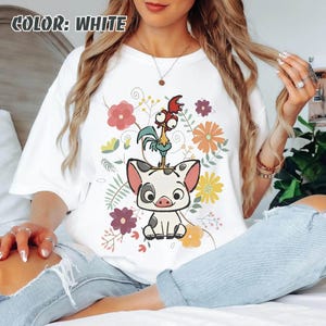 Puede incluir: Camiseta blanca con un dise&ntilde;o de cerdo y gallo de dibujos animados, sobre un fondo de flores y hojas coloridas. El texto "COLOR: WHITE" es visible. El dise&ntilde;o incorpora tonos rosas, naranjas, amarillos y verdes.