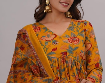 May include: Mustard yellow floral print dress with a matching scarf. The dress features a V-neck and long sleeves. The floral pattern includes red, blue, and green accents. Gold-colored earrings complete the look.