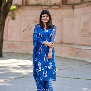May include: A woman wearing a blue and white printed kurta with a matching dupatta. The kurta has a floral design and the dupatta is sheer. The woman is standing in front of a brick wall.