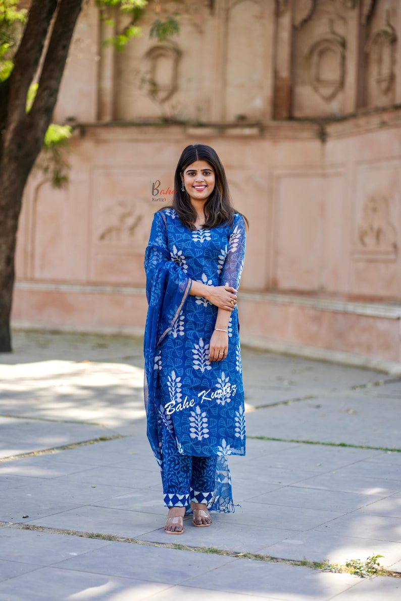 May include: A woman wearing a blue and white printed kurta with a matching dupatta. The kurta has a floral design and the dupatta is sheer. The woman is standing in front of a brick wall.