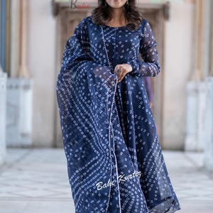 May include: A navy blue dress with a white print and a matching dupatta. The dress has a long sleeve and a flared skirt. The dupatta has a pearl trim.
