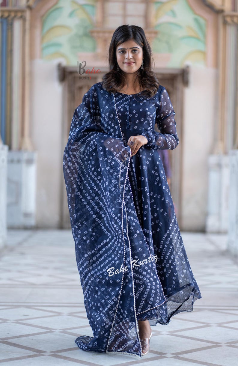 May include: A navy blue dress with a white print and a matching dupatta. The dress has a long sleeve and a flared skirt. The dupatta has a pearl trim.