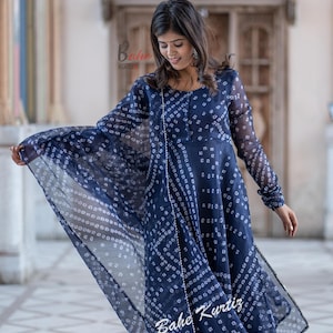 May include: A navy blue long-sleeved dress with a white print. The dress has a flowing silhouette and is paired with a matching dupatta. The dress is adorned with pearl embellishments. The model is wearing silver sandals.