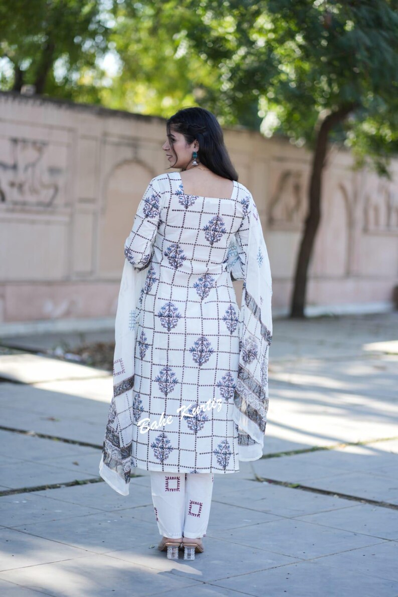 May include: A white and blue patterned salwar kameez with a square neckline and a dupatta. The salwar kameez has a checkered pattern with floral designs. The dupatta is a sheer white fabric with a floral border.