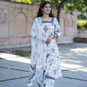 May include: A white cotton kurta with a geometric pattern and a matching white palazzo pant. The kurta has a square neckline and three-quarter sleeves. The palazzo pants have a wide leg and are embroidered with a geometric pattern. The model is wearing a white dupatta with a geometric pattern.
