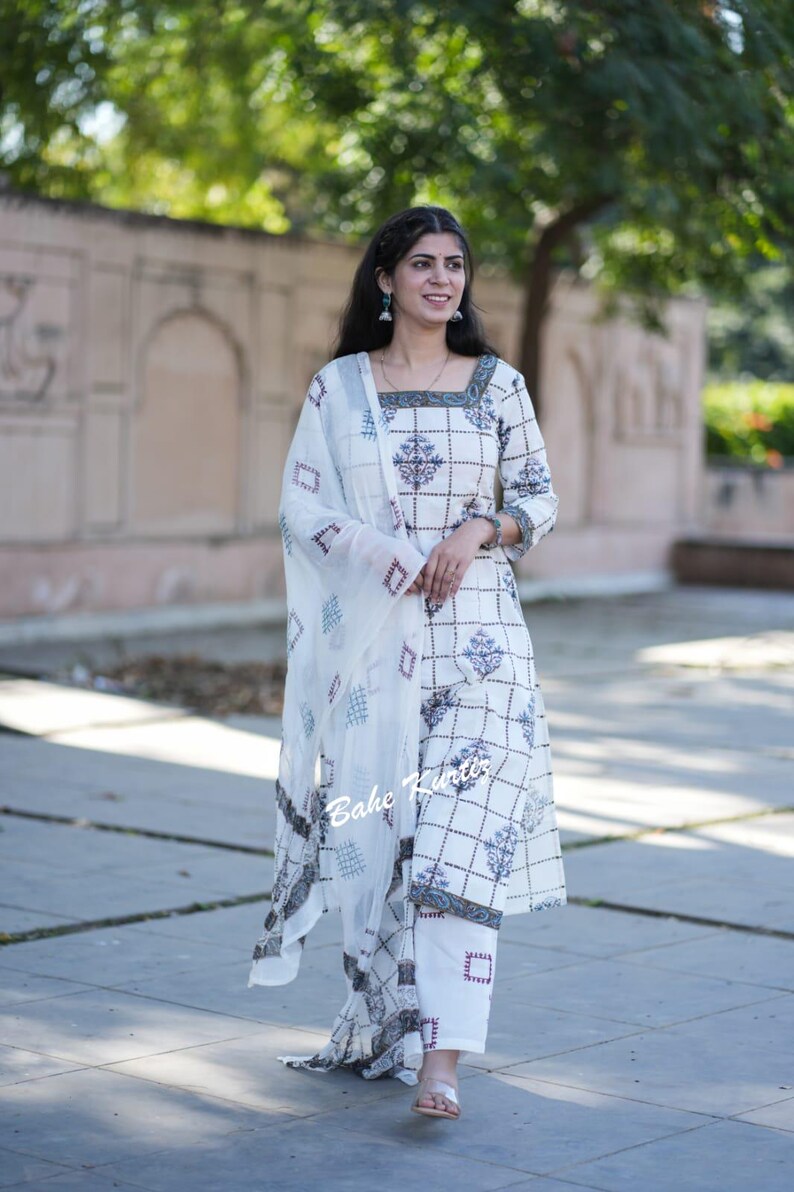 May include: A white cotton kurta with a geometric pattern and a matching white palazzo pant. The kurta has a square neckline and three-quarter sleeves. The palazzo pants have a wide leg and are embroidered with a geometric pattern. The model is wearing a white dupatta with a geometric pattern.