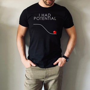 May include: A black t-shirt with the text "I HAD POTENTIAL" in white lettering. A white line curves downward with a red circle at the end of the line.